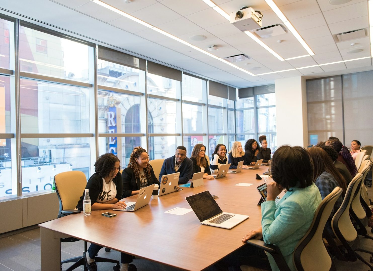 Skill Loop Collective Who We Are Page Diverse group of professionals in a meeting room discussing with laptops and notebooks.