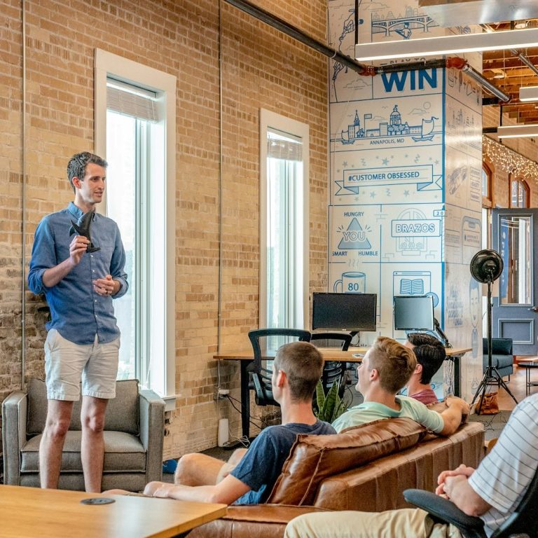 Skill Loop Collective Who We Are Page A man speaks to a small audience in a modern office setting.